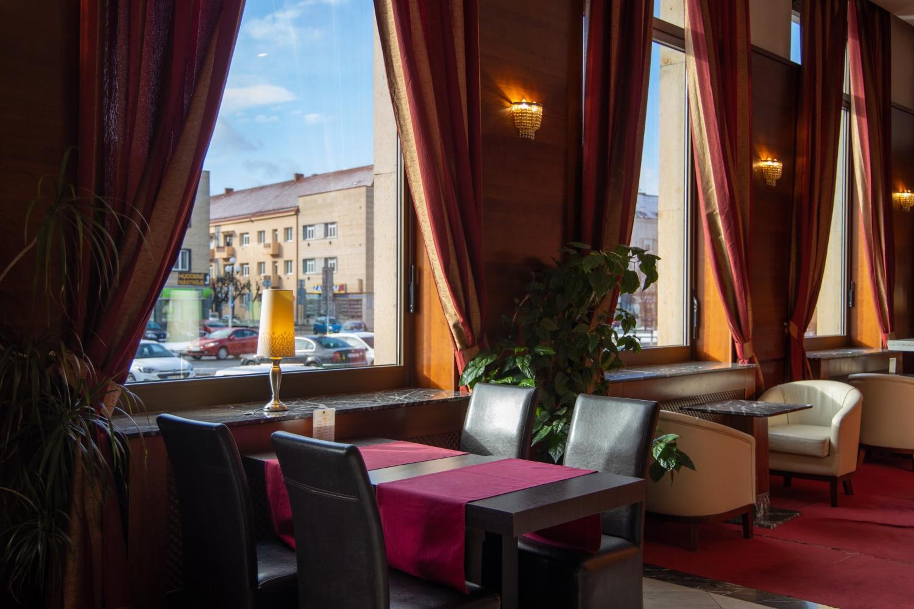 A restaurant interior with a table set for two, a potted plant, and a view of the street outside.