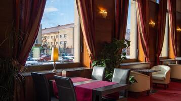 A restaurant interior with a table set for two, a potted plant, and a view of the street outside.