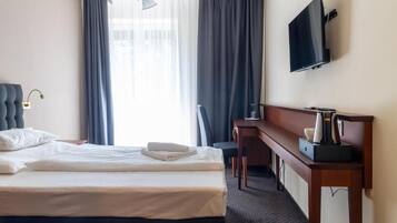 Ett hotellrum med en säng, ett skrivbord, en stol, en tv och ett fönster med gardiner.