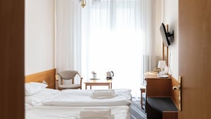 Een hotelkamer met een bed, een stoel, een bureau, een televisie en een raam met gordijnen.