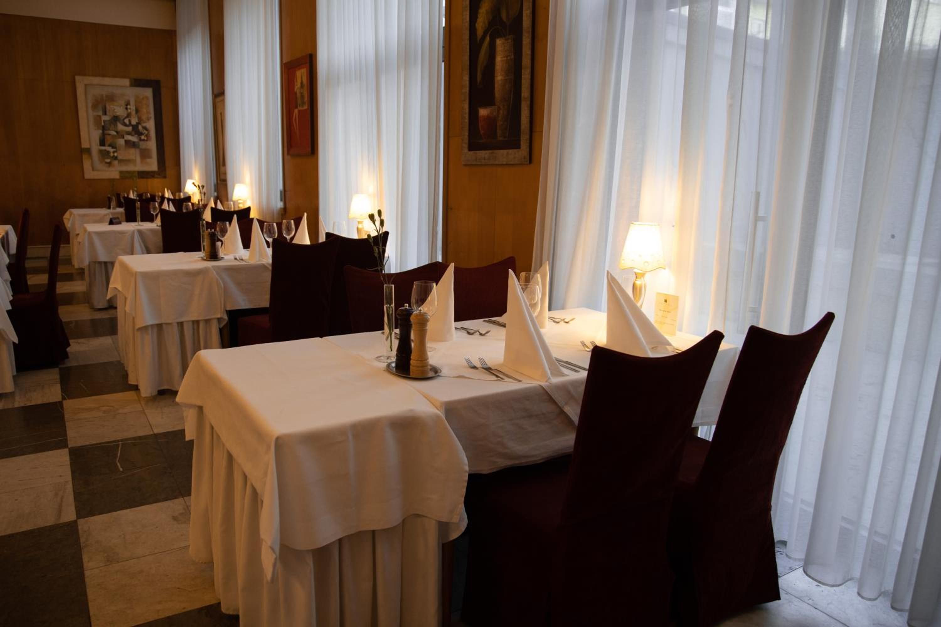 A dining area with tables set for two, white tablecloths, and dark chairs.