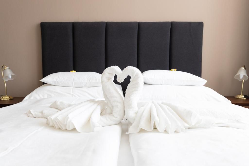 A neatly made bed with a heart-shaped towel arrangement on a bed with a dark headboard.