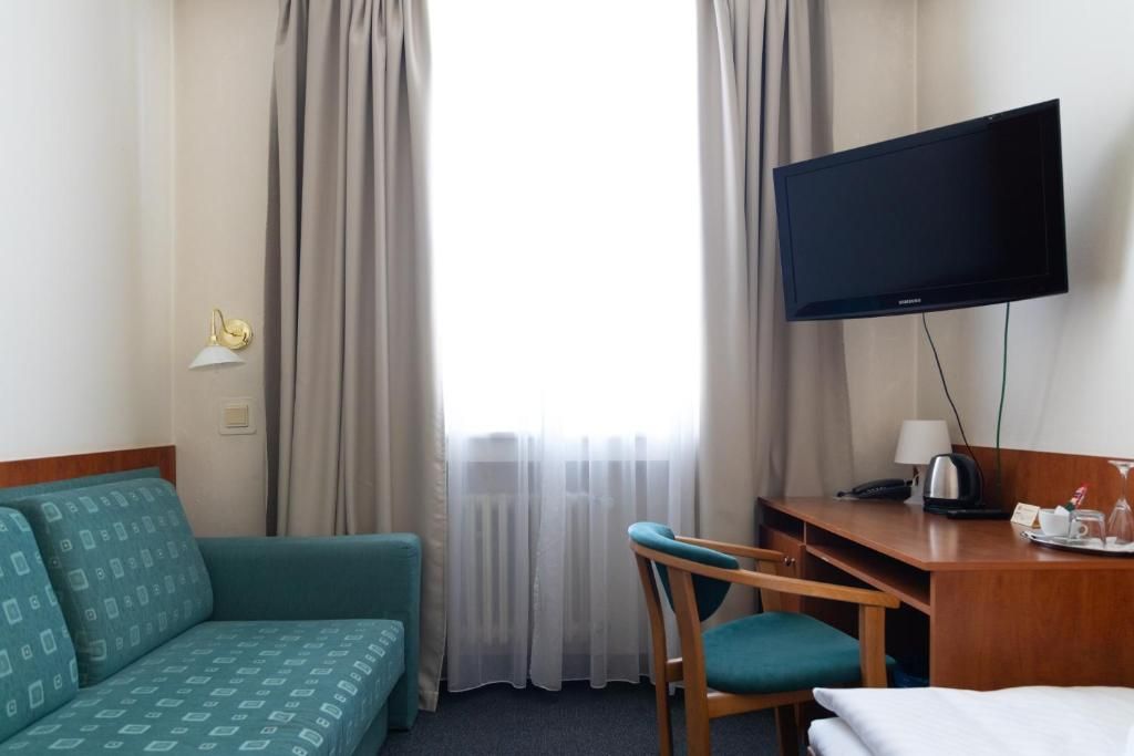 A hotel room with a sofa, a desk, a television, and a window with curtains.