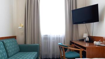 A hotel room with a sofa, a desk, a television, and a window with curtains.