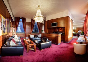 A hotel lobby with leather sofas, a wooden reception desk, a chandelier, and a red carpet. - Hotel Poľana (Zvolen)