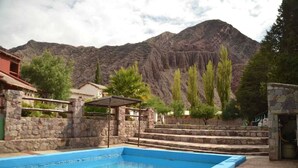 Una piscina con escalones de piedra que la bordean, rodeada de árboles y una montaña al fondo.