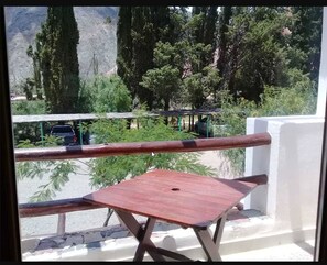 Varanda com mesa de madeira e vista para área de estacionamento e vegetação.
