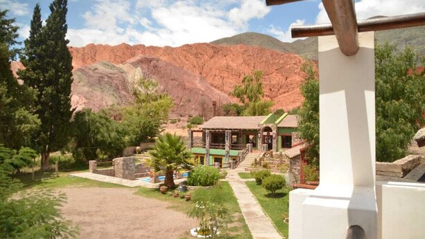 Un edificio rústico con techo verde, rodeado de un jardín cuidado y con montañas al fondo.