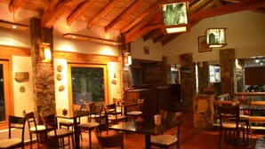Un restaurante acogedor con vigas de madera, pilares de piedra y una zona de bar. Mesas y sillas dispuestas para comer.