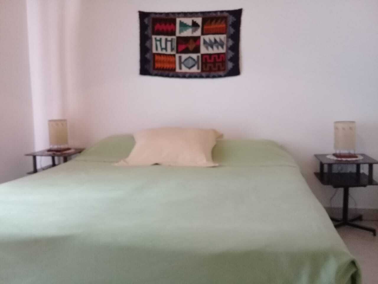 A simple room with a bed, a wall tapestry, and two nightstands with lamps.