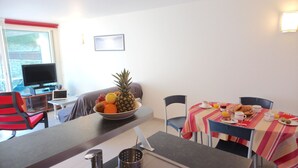 A dining area with a table set for breakfast, a bowl of fruit on the counter, and a television in the background. - Le Grand Large - house in Locmariaquer centre, 4p (Locmariaquer)