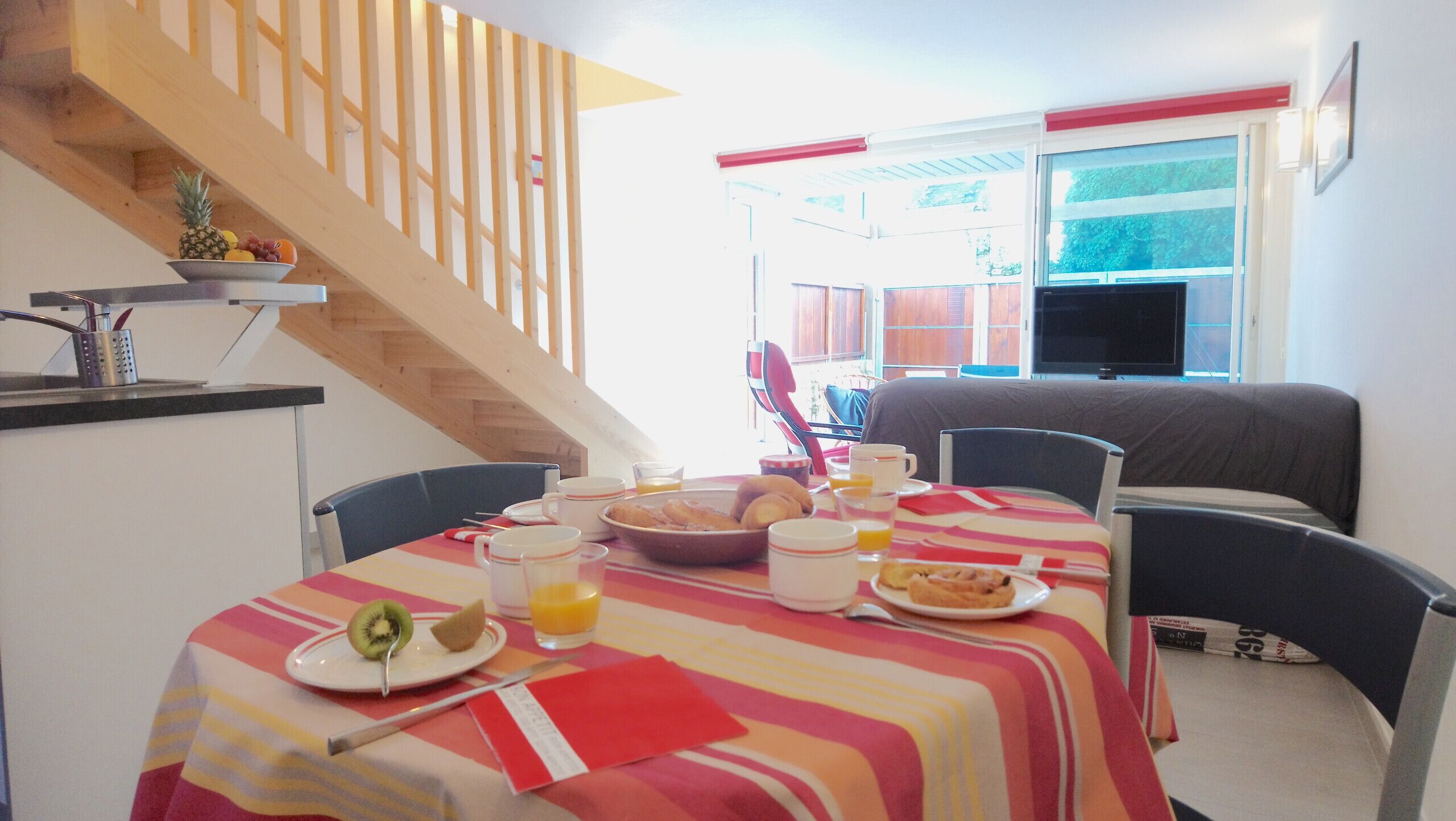Una zona de dinar amb una taula preparada per l'esmorzar, incloent plats de menjar, tasses i un plat de fruita.