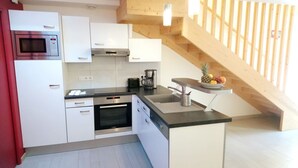 A modern kitchen with white cabinets, a built-in oven, a microwave, and a coffee maker. There's a wooden staircase to the right. - Le Grand Large - house in Locmariaquer centre, 4p (Locmariaquer)
