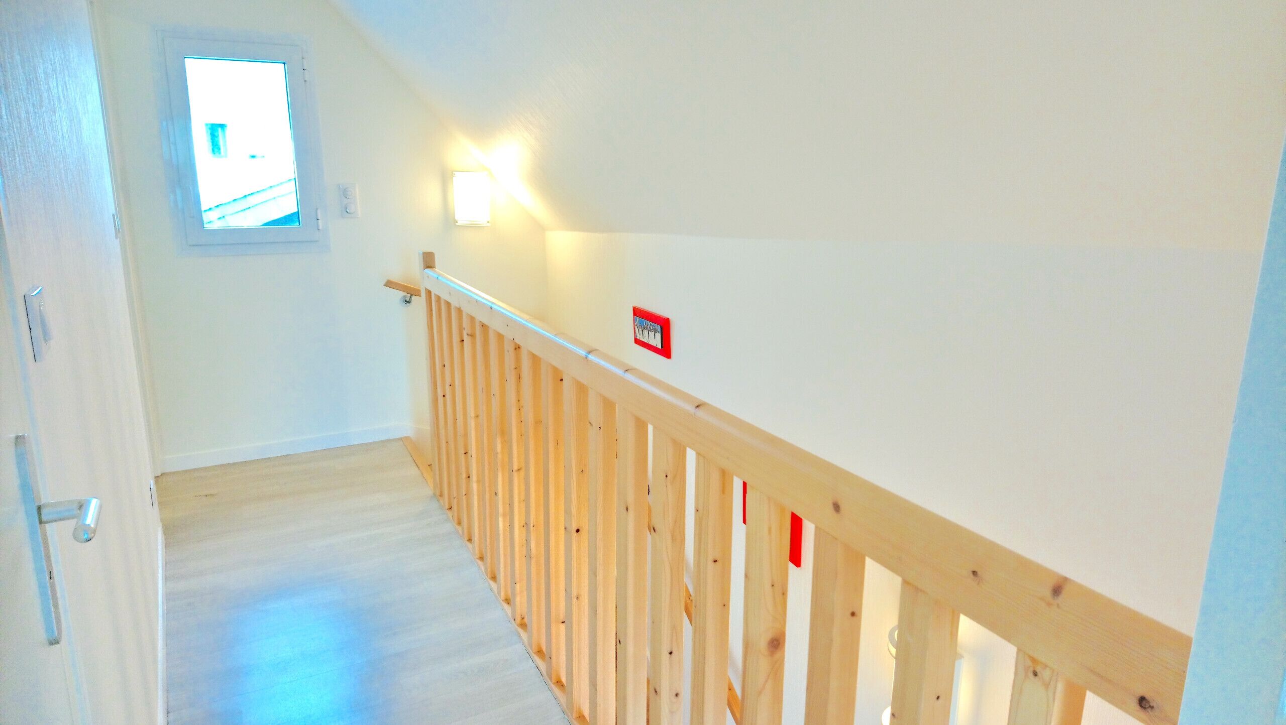 A narrow staircase with a wooden handrail and a small window at the top.