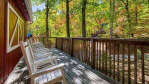 A wooden deck with white chairs, surrounded by trees with autumn foliage. - Four Bears Den, Free Attraction Tickets, Hot Tub, Arcade Game, Gatlinburg, WIFI! (Gatlinburg)