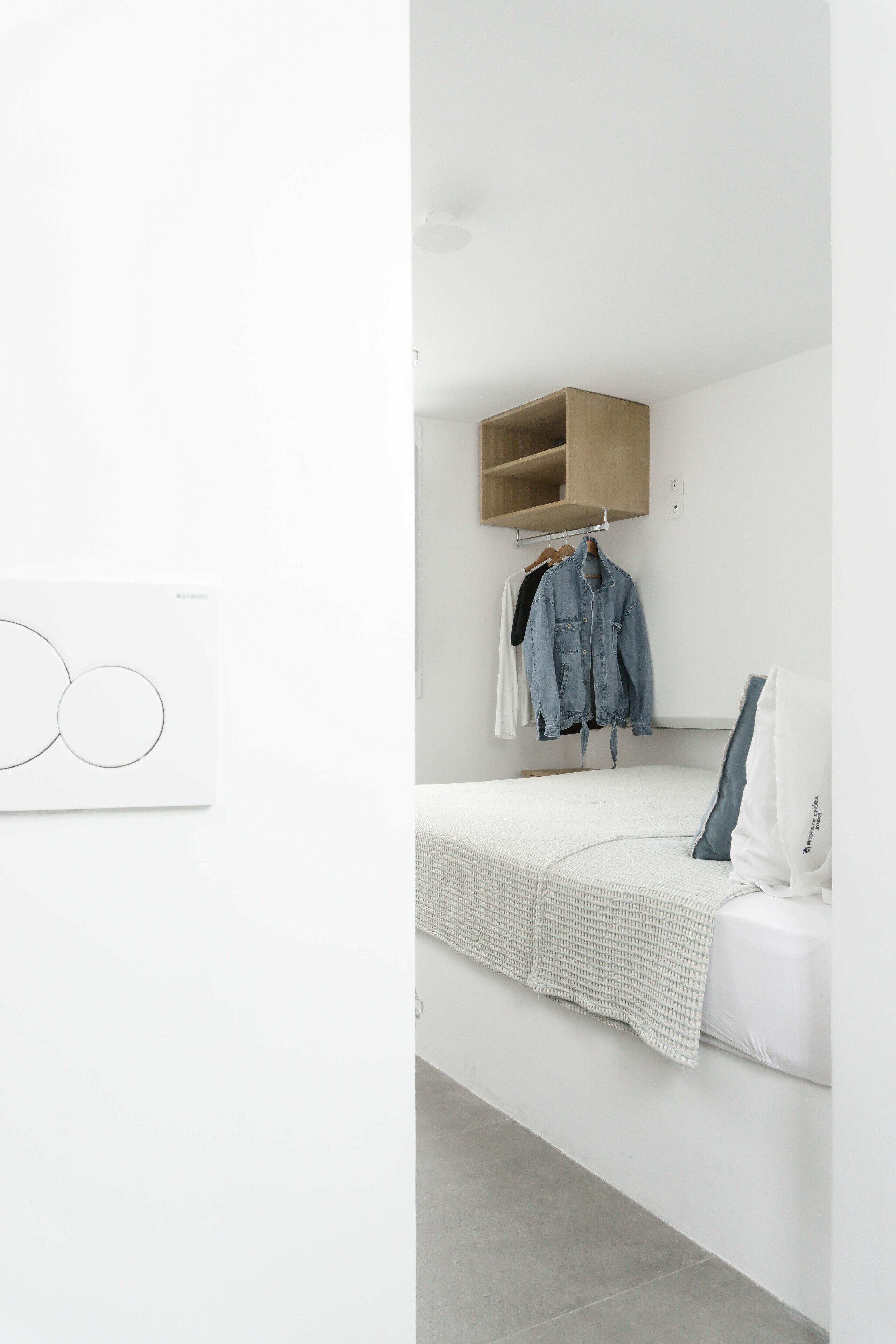 A minimalist bedroom with a bed, a wooden shelf, and a wall-mounted artwork.
