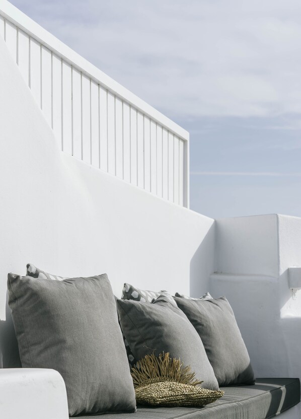 A modern outdoor seating area with a white railing and grey cushions.