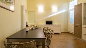 Een eetgedeelte met een tafel, stoelen, een fles wijn en een televisie op een kast.
