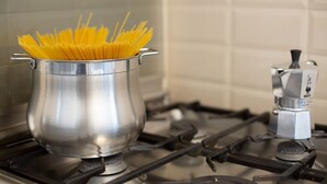 Een roestvrijstalen pan op een kookplaat met ongekookte spaghetti.