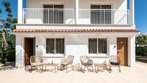 Ein zweigeschossiges Gebäude mit Balkon, weißem Außenbau und Ziegeldach. Auf dem Erdgeschoss stehen vier Korbstühle und ein kleiner Tisch.