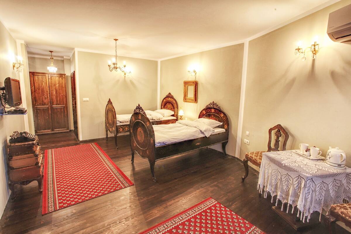 A room with two wooden beds, a small table with a teapot, and a red and white patterned rug.