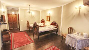 A traditional room with a bed, two chairs, a table with a teapot, and a red patterned rug.