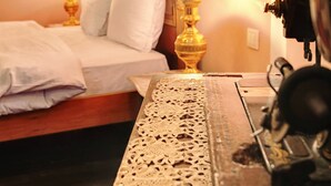 A bedroom with a bed, a wooden nightstand, a lace table runner, a chandelier, and a wall-mounted radiator.