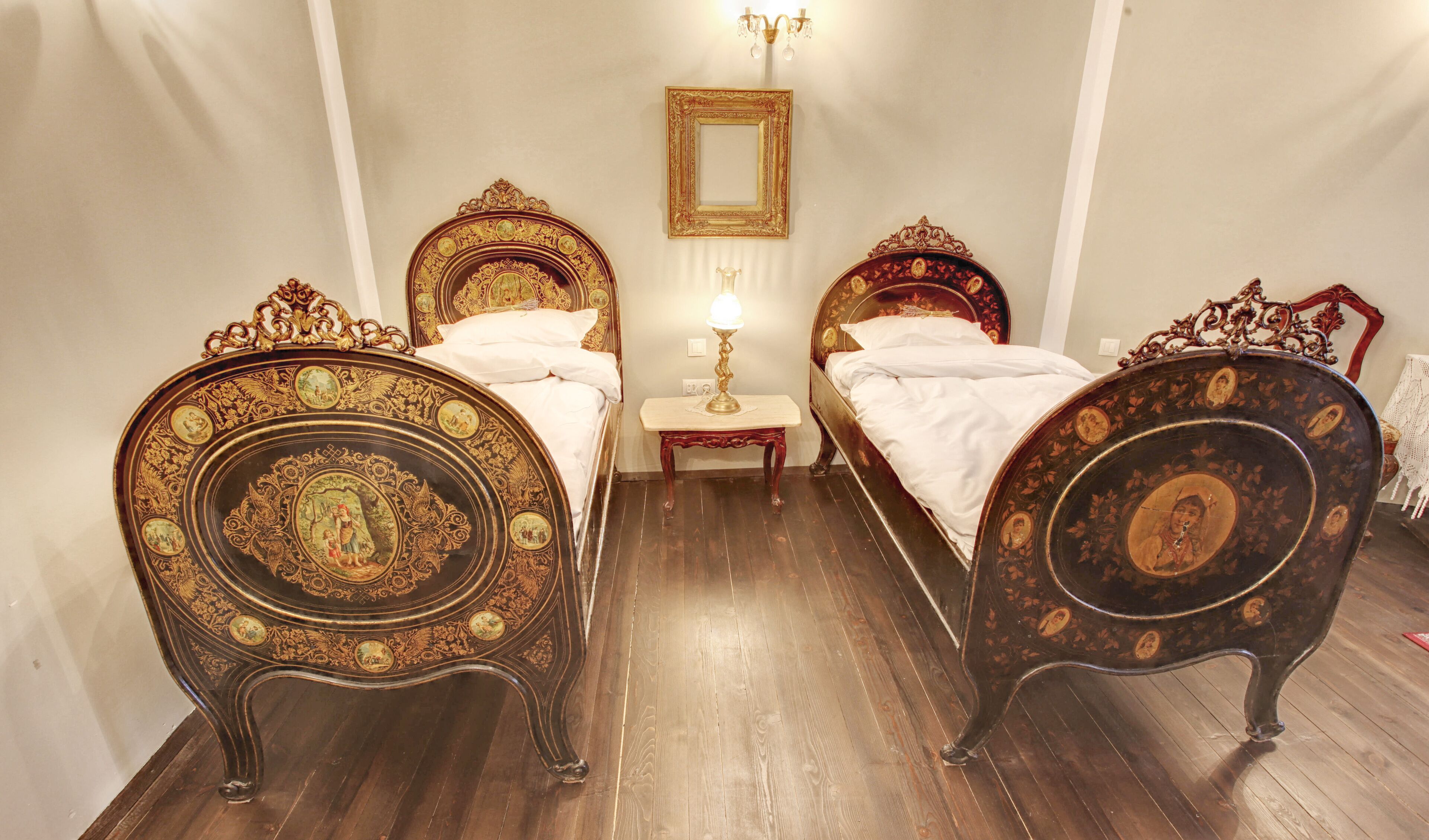 A room with two ornate beds, a small table with a lamp, and a mirror on the wall.