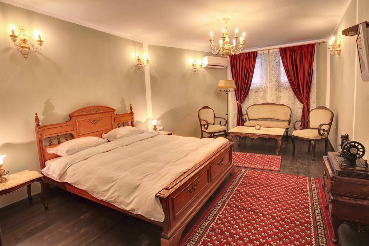 A traditional bedroom with a wooden bed, two chairs, a small table, and a red patterned rug.
