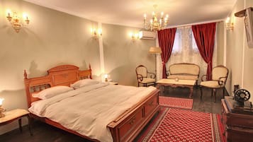Ein traditionell eingerichtetes Schlafzimmer mit einem hölzernen Bett, zwei Stühlen, einem kleinen Tisch und einem roten Teppich mit Muster.