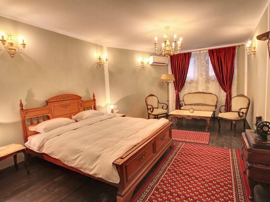 Ein traditionell eingerichtetes Schlafzimmer mit einem hölzernen Bett, zwei Stühlen, einem kleinen Tisch und einem roten Teppich mit Muster.