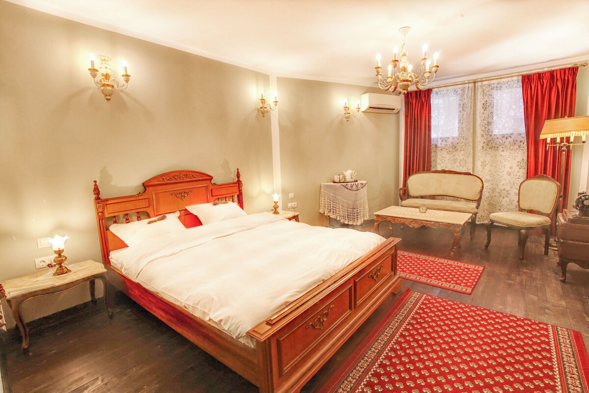 A hotel room with a wooden bed, a sitting area with chairs, a table, and a red patterned rug.