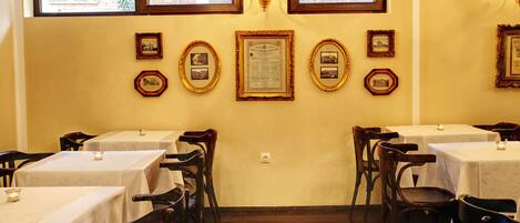 A dining area with tables and chairs, framed pictures on the wall, and a chandelier.