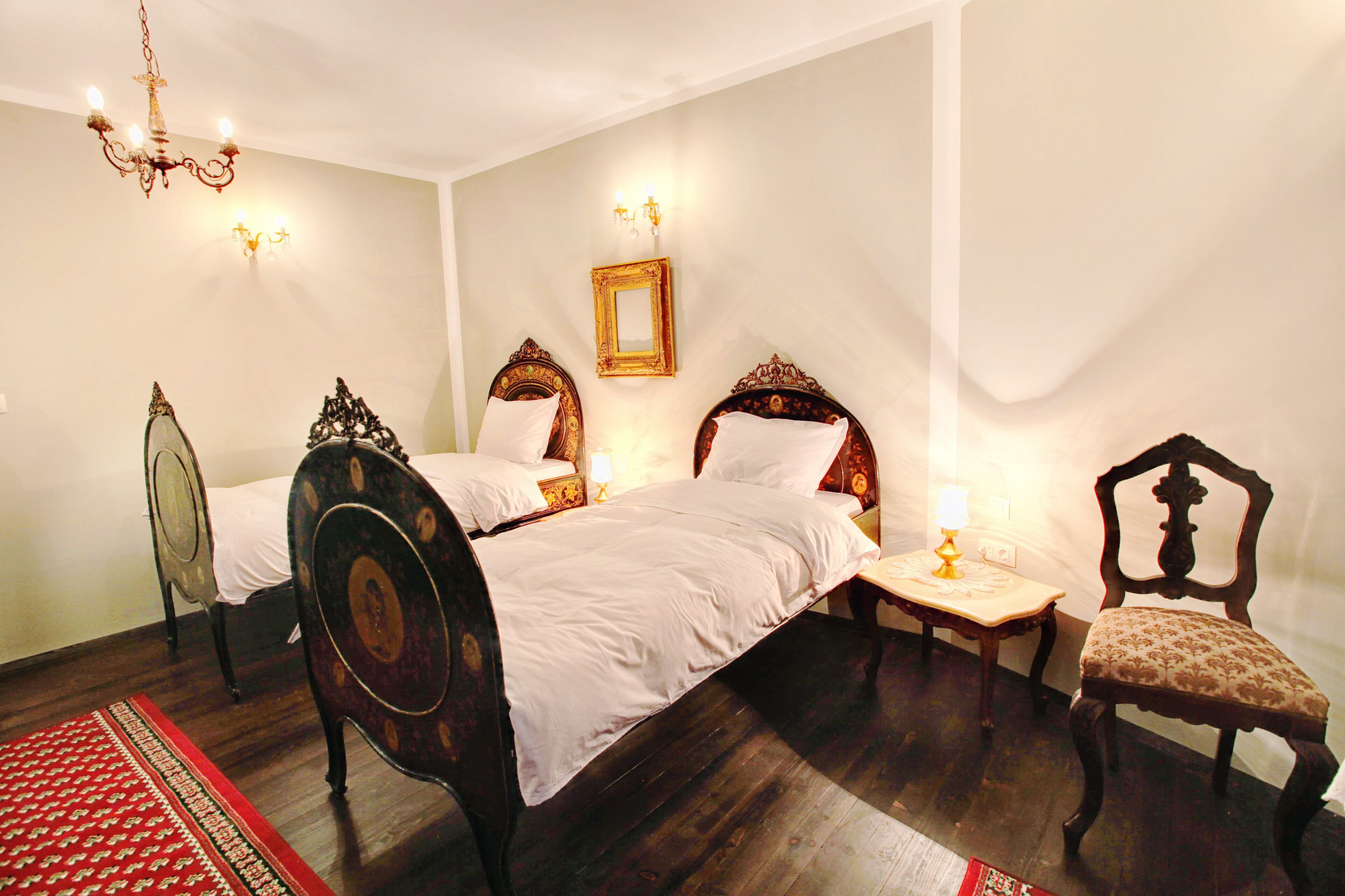Ein Schlafzimmer mit zwei Betten, einem Sessel, einem Nachttisch, einer Kristallleuchtre und einem an der Wand befestigten Spiegel.