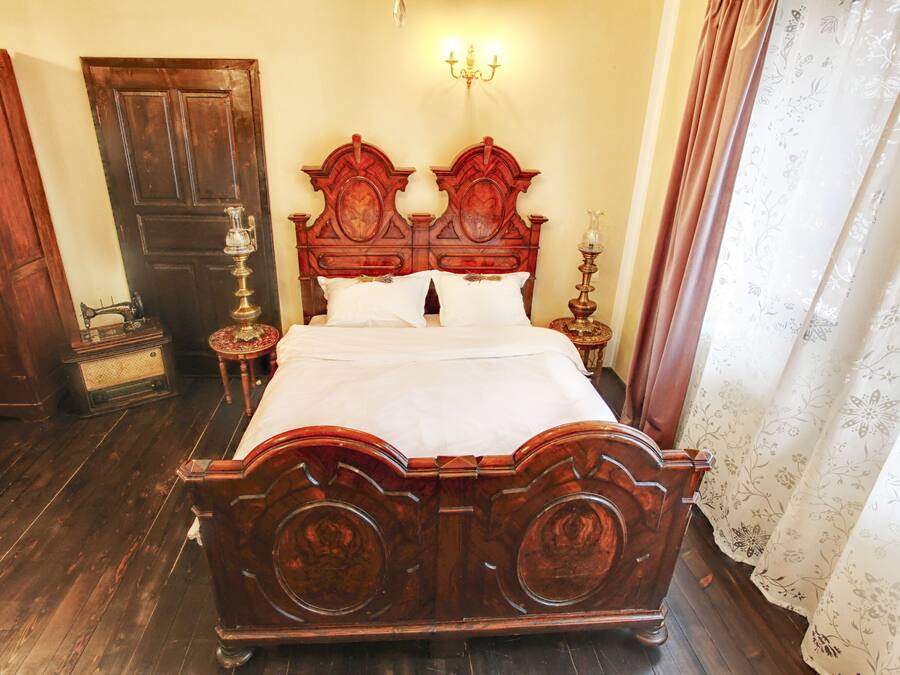 A traditional wooden bed with a headboard, a bedside table with a lamp, and a door in the background.