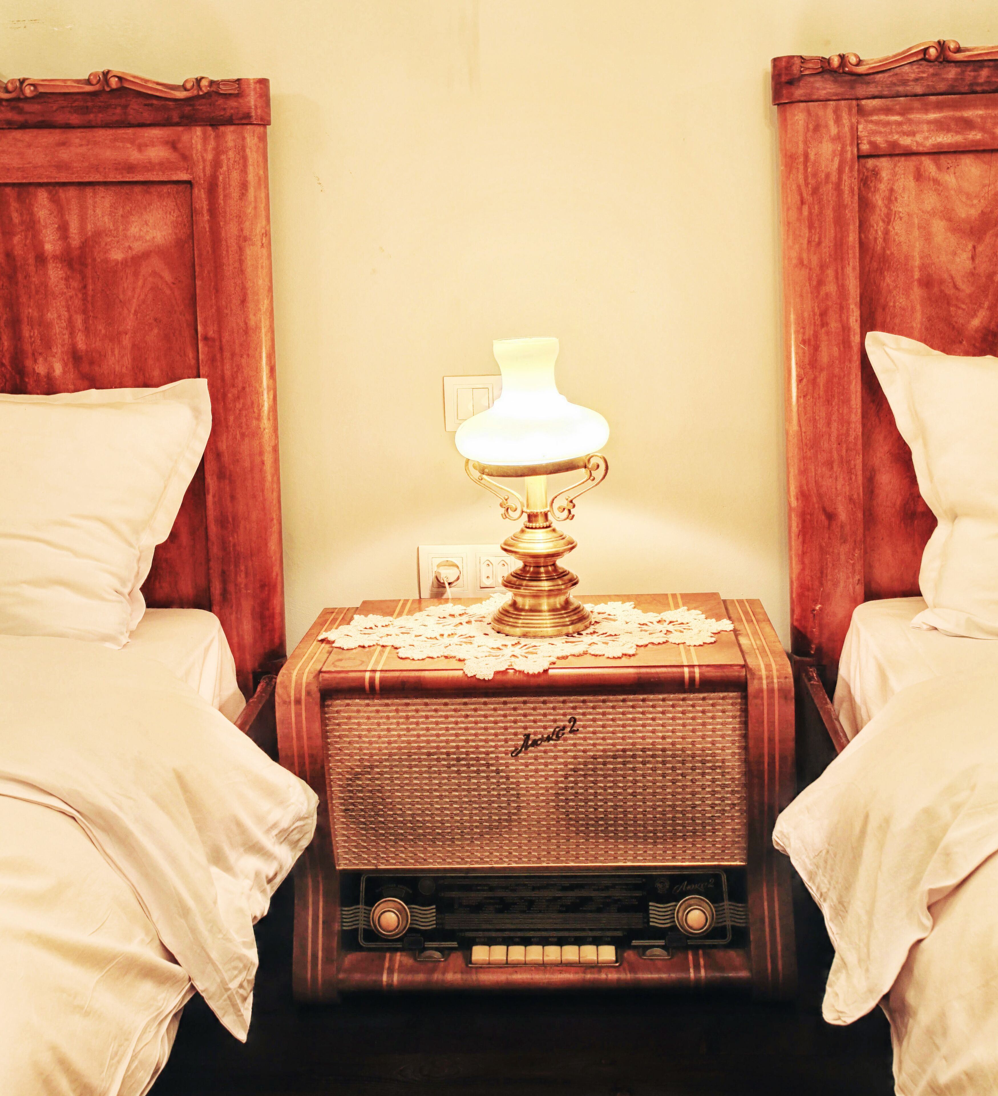 A room with two beds, a nightstand with a lamp, and a vintage radio.