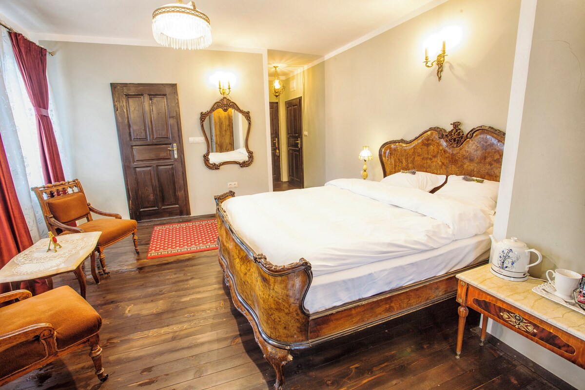 A traditional bedroom with a wooden bed, a small table with chairs, a red rug, and a chandelier.