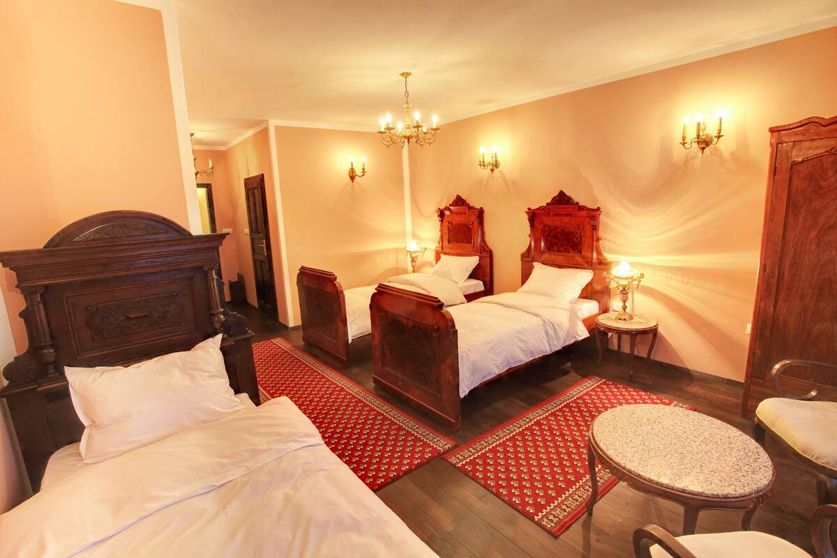 A hotel room with two wooden beds, a red patterned rug, a round table, and a chair.