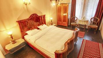 A traditional bedroom with a large wooden bed, a wardrobe, a small table with chairs, and a chandelier.