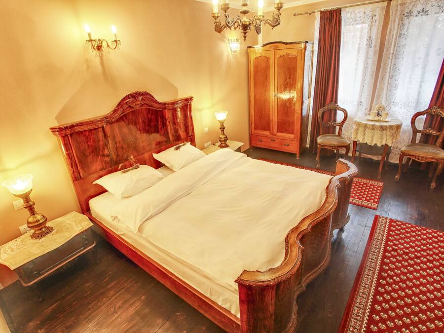 A traditional bedroom with a large wooden bed, a wardrobe, a small table with chairs, and a chandelier.