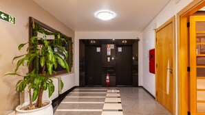 A hallway with a potted plant, a fire extinguisher, and a door with a sign.