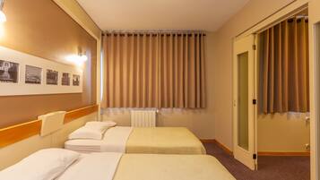 Een hotelkamer met twee bedden, een wandlamp, een radiator en een deur voorzien van gordijnen.