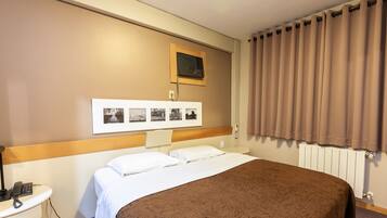 Una camera d'hotel con un letto, un comodino con lampada, un condizionatore d'aria a parete e una finestra con tende.