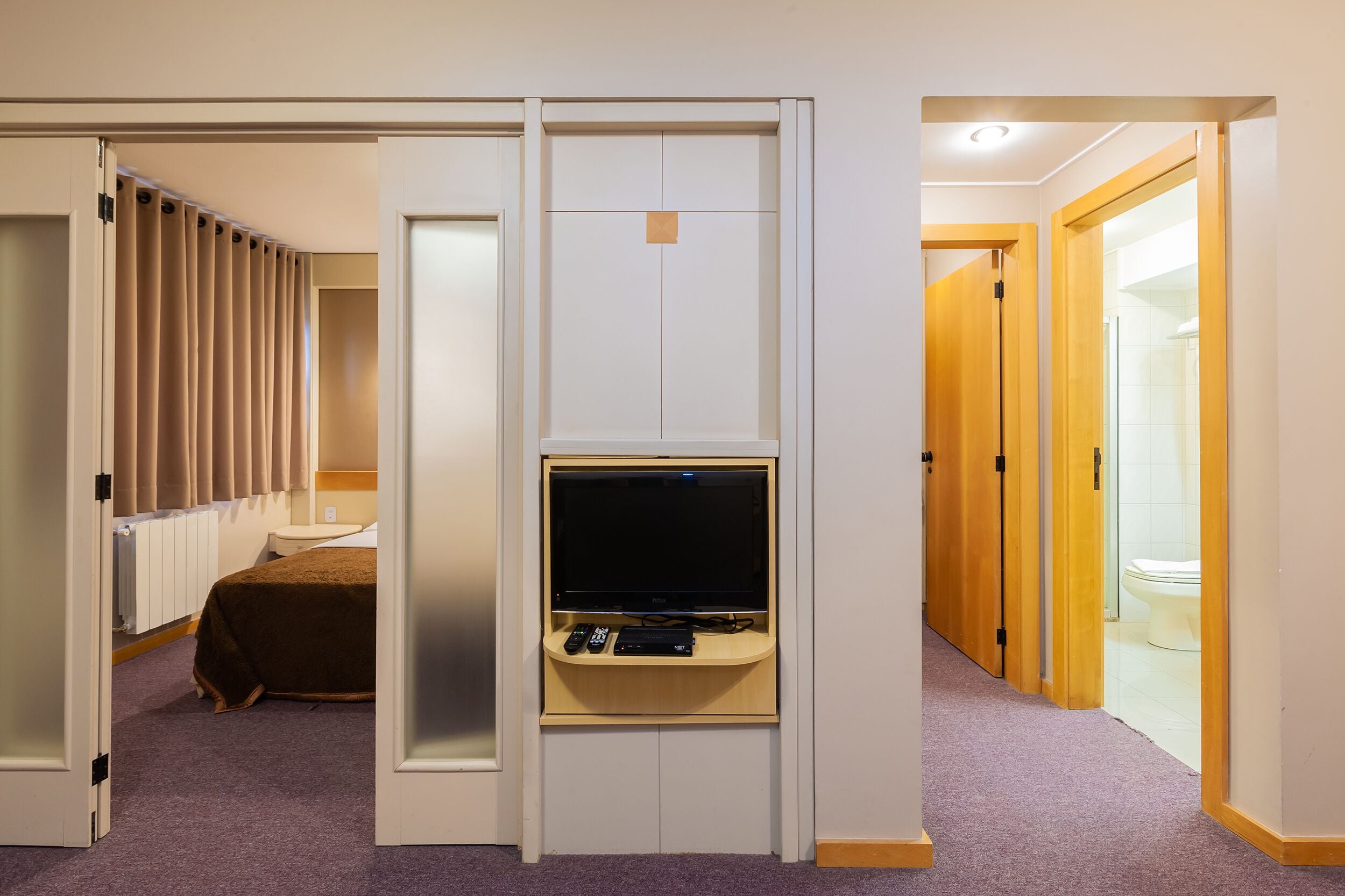 A hotel room with a bed, a TV, and a bathroom visible through an open door.