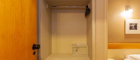 A small, compact bathroom with a wooden door, a white toilet, a small cabinet, and a shelf above the toilet.