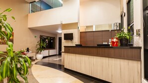 A modern hotel lobby with a reception desk, potted plants, and a large mirror.