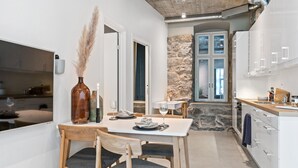 A modern kitchen with white cabinets, a stone accent wall, and a dining area with wooden chairs and a white table. - Aalesund City Apartment (Ålesund)