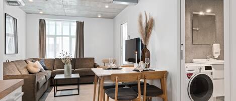 A modern living room with a sofa, dining table, chairs, and a washing machine.