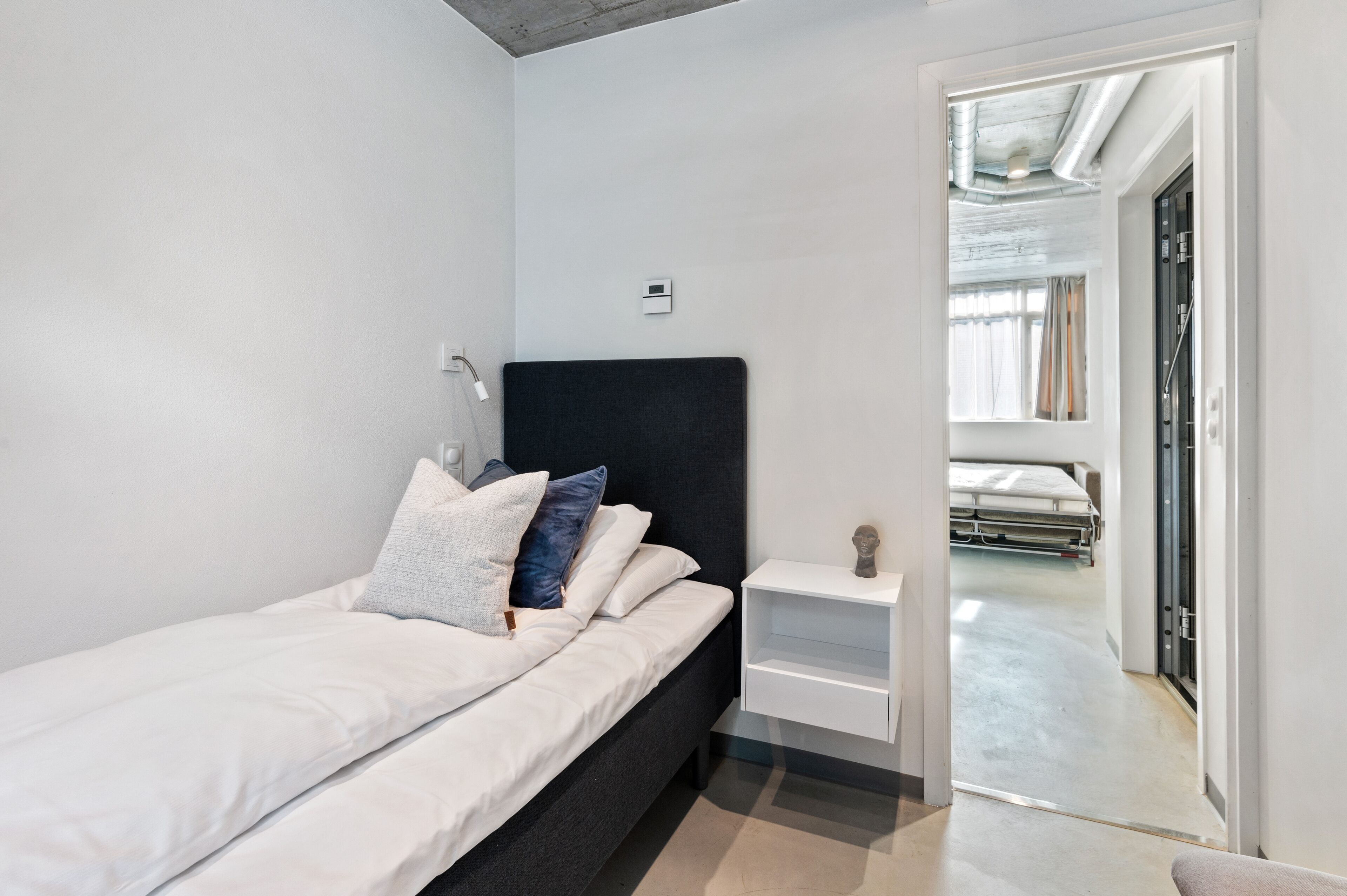 Une chambre moderne avec un lit, une table de chevet et une vue sur un couloir menant à une autre pièce.