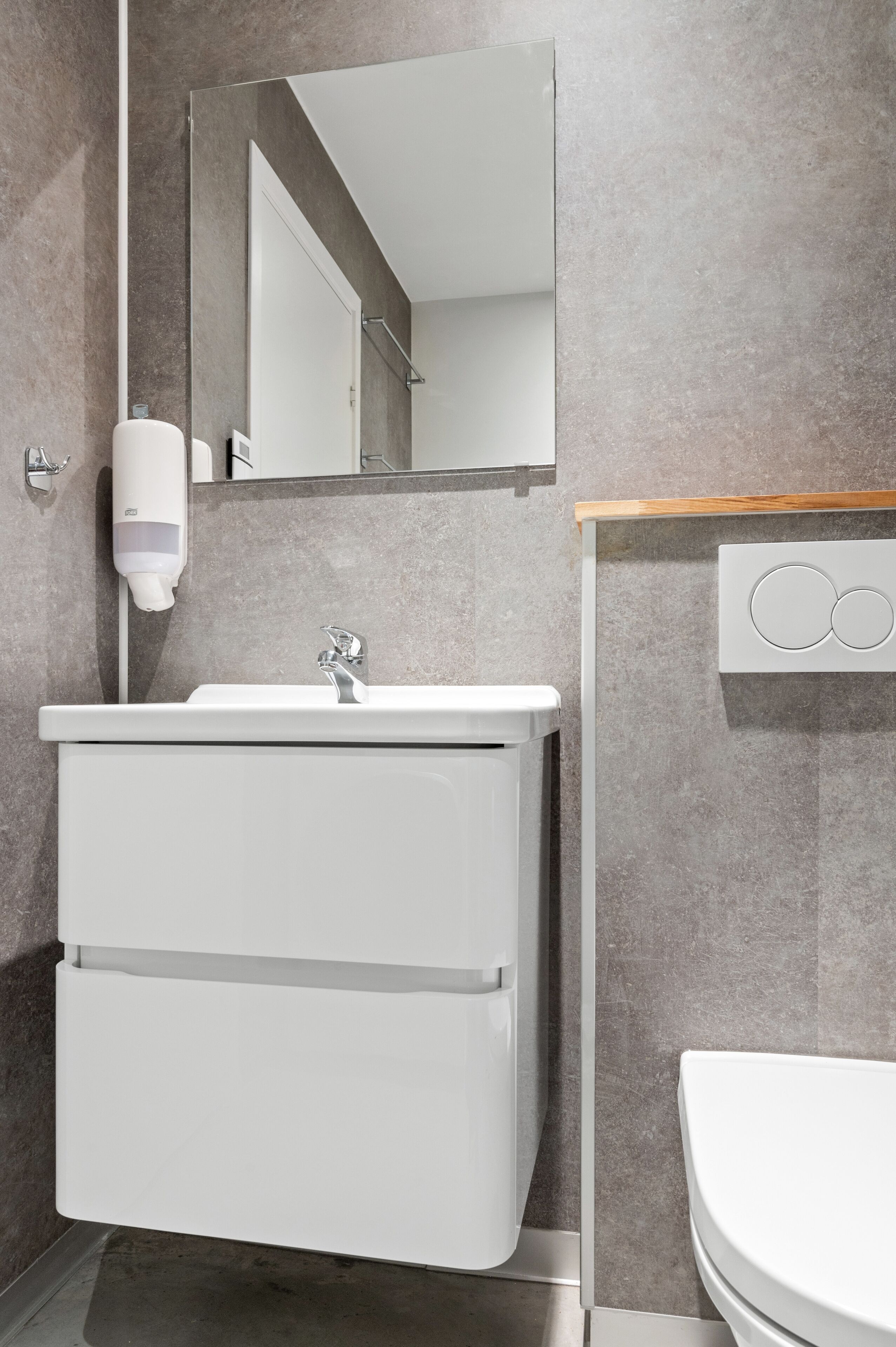 Un baño moderno con lavamanos, espejo y retrete blancos.